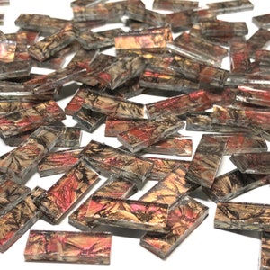 May include: A pile of small, rectangular glass tiles with a marbled pattern in shades of brown, gold, and pink. The tiles are iridescent and have a slightly metallic sheen.