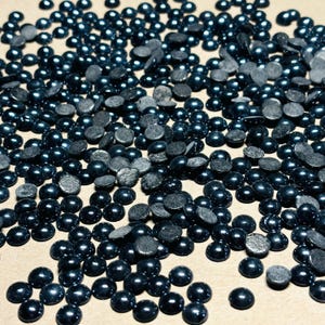 May include: A large quantity of dark blue round rhinestones, scattered on a light brown surface.