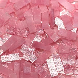 May include: A collection of small, rectangular, pink glass mosaic tiles. The tiles vary in shade from light to medium pink and have a slightly textured surface. These tiles are suitable for various craft and decorative projects.