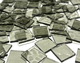 May include: A pile of small, square, translucent glass tiles in a light gray color. The tiles are arranged in a random pattern and are slightly overlapping.