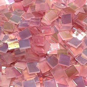 Op de afbeelding: Een stapel iriserende roze glazen mozaïektegels. De tegels zijn vierkant en hebben een licht doorschijnende uitstraling.