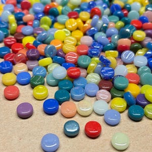 May include: A large collection of small, round, flat glass tiles in a vibrant assortment of colors including red, yellow, blue, green, purple, and orange. Each tile features a smooth, glossy finish and a uniform circular shape, scattered.