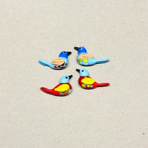 May include: Four colorful bird figurines. Two birds are blue with orange and brown accents, and two are red with yellow and blue accents. Each bird has a black beak and is set against a neutral background.