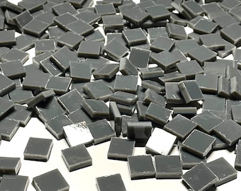 May include: A large quantity of small, gray, square tiles. The tiles are scattered on a white surface.