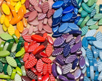 May include: A colourful collection of oval glass beads, arranged in a rainbow pattern. The beads range in colour from yellow to purple. Some of the beads have a textured, striped design, adding visual interest to the collection. The beads are measured in centimetres.