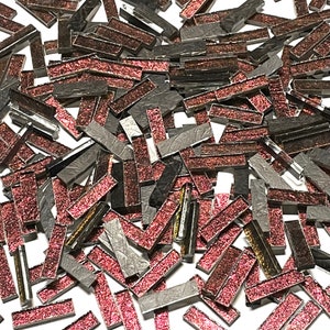 May include: A pile of small, rectangular glass tiles with a glittery finish. The tiles are a mix of dark gray and a deep red color.