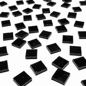 以下が含まれることがあります： 白い表面に散らばった黒い正方形のタイルのコレクション。タイルは光沢があり、光を反射しています。