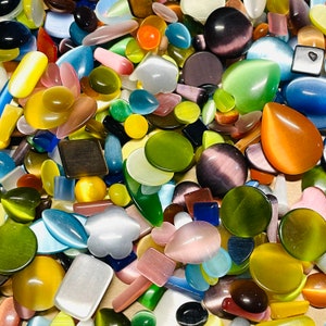 May include: Assortment of colorful, smooth, and polished gemstone cabochons in various shapes and sizes. The cabochons are made of agate, jasper, and other natural stones.