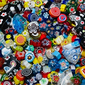 Puede incluir: Una colección de cuentas de vidrio de colores con varios patrones y diseños. Las cuentas están hechas de vidrio de Murano y presentan remolinos, flores y formas geométricas.