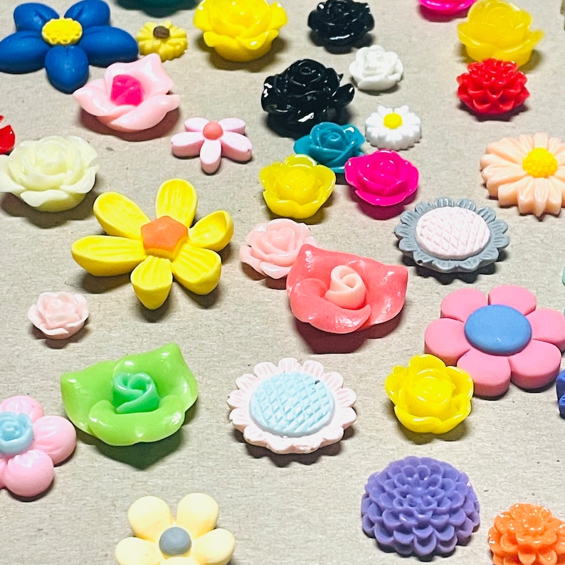 May include: Assortment of colorful resin flower embellishments in various shapes and sizes. The flowers are made of a smooth, glossy material and feature intricate details.