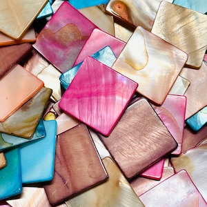 May include: A collection of square-shaped mother of pearl tiles in various colors including vibrant pink, soft blue, iridescent white, and deep brown. Each tile features a smooth, polished surface with natural pearlescent textures and variations.