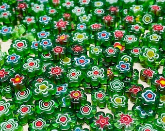 Könnte beinhalten: Eine Sammlung bunter, glasiger Knöpfe in Blumenform mit grünen, weißen, roten und blauen Akzenten. Die Knöpfe sind in einem zufälligen Muster angeordnet.