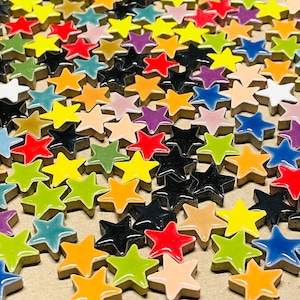 Könnte beinhalten: Eine Sammlung von bunten, sternförmigen Keramikfliesen in verschiedenen Blautönen, Grün-, Rot-, Gelb-, Orange- und Schwarztönen. Die Fliesen sind in einem zufälligen Muster angeordnet und bilden ein optisch ansprechendes Mosaik.