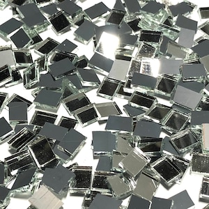 May include: A pile of small, square, silver mirror tiles. The tiles are scattered on a white surface.