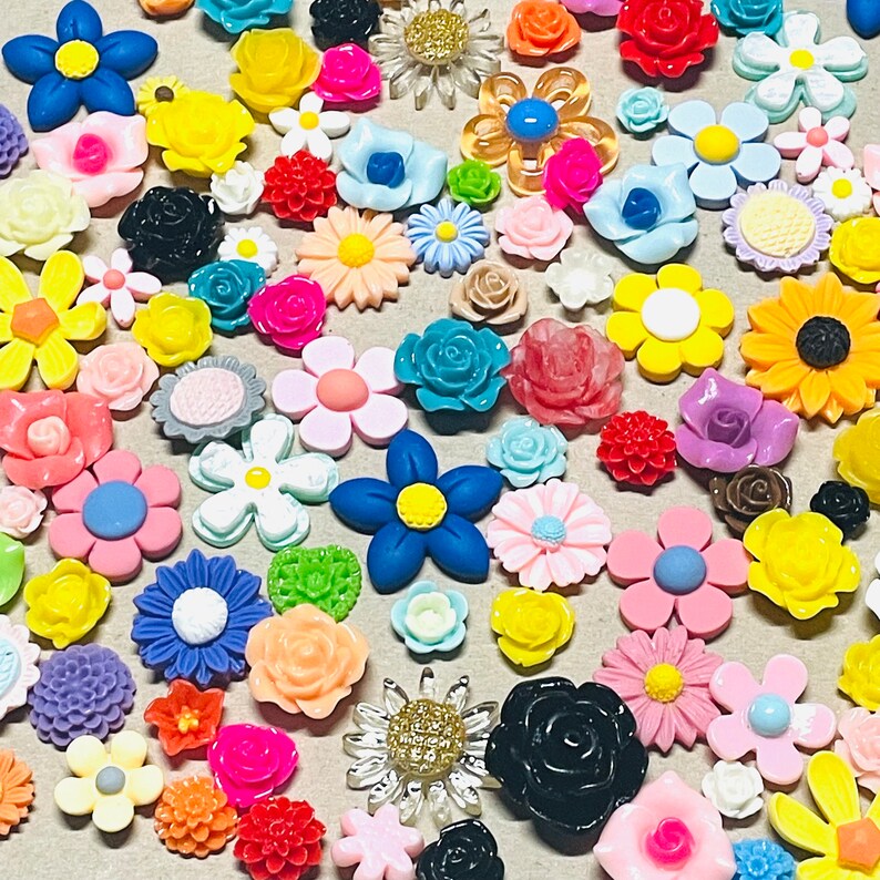 May include: Assortment of colorful resin flower embellishments in various shapes and sizes. The flowers are made of a shiny, smooth resin and feature a variety of colors, including pink, blue, yellow, green, and red.