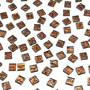 May include: A scattering of small, square, copper-colored mosaic tiles. Each tile has a textured, metallic appearance, reflecting light. The tiles are scattered across a white background, creating a pattern.