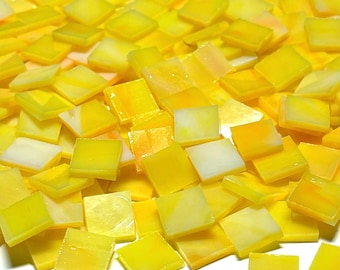 May include: A collection of small, square glass mosaic tiles in various shades of yellow. Each tile features a smooth, flat surface with semi-translucent qualities and subtle white or lighter yellow marbled patterns throughout the glass material.