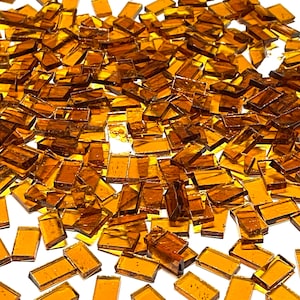 May include: A large quantity of small, rectangular, amber-colored glass tiles. The tiles are scattered on a white surface.