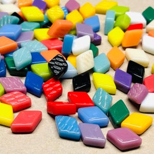 May include: A selection of colourful, diamond-shaped glass mosaic tiles in shades like yellow, orange, blue, red, and purple. Some tiles have textured surfaces. The tiles are scattered, creating a vibrant and artistic display.
