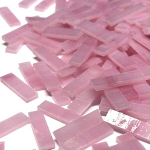 May include: A pile of small, rectangular, translucent pink glass tiles. The tiles are scattered, with varying angles and slight variations in color. These tiles are suitable for mosaic art projects.