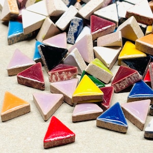 May include: A collection of colorful, triangular mosaic tiles in various shades, including red, yellow, blue, and pink. The tiles have a glossy finish and are arranged randomly, showcasing their diverse hues and textures. The tiles are approximately 1 inch in size.