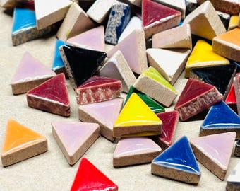 Può includere: Una collezione di tessere di mosaico triangolari colorate in varie tonalità, tra cui rosso, giallo, blu e rosa. Le tessere hanno una finitura lucida e sono disposte in modo casuale, mostrando le loro diverse tonalità e trame. Le tessere misurano circa 2,5 cm.