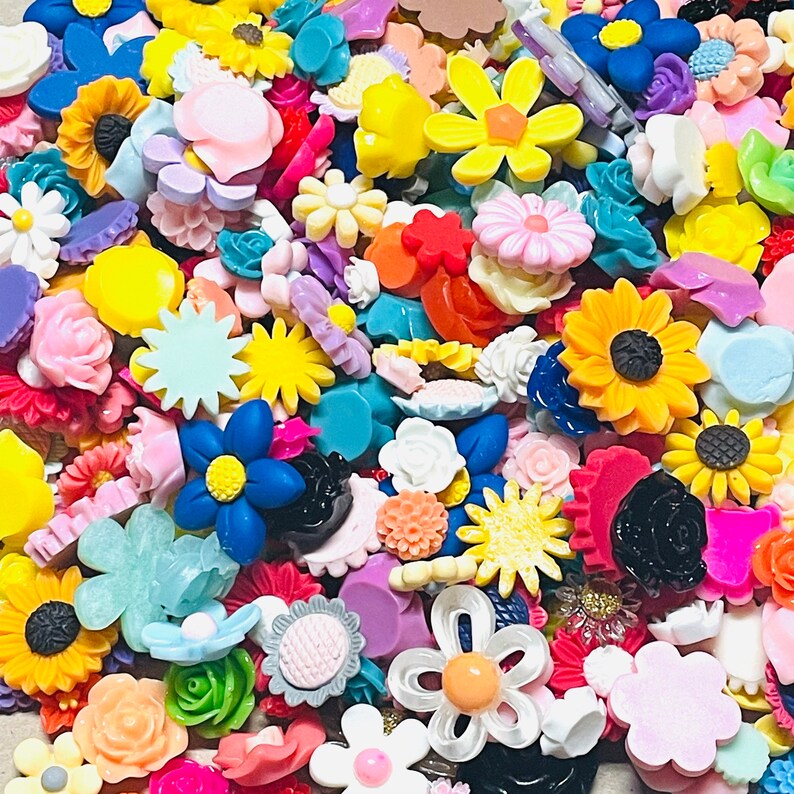 May include: A large collection of colorful resin embellishments in various shapes, including flowers, stars, and geometric designs. The embellishments are perfect for crafting and adding a touch of whimsy to projects.