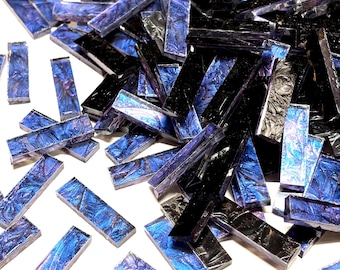 Puede incluir: Una colección de azulejos de vidrio rectangulares que presentan una mezcla de superficies de color negro profundo y azul iridiscente. Los azulejos tienen un acabado liso y reflectante, con algunas piezas que muestran un patrón texturizado y arremolinado en tonos azules y morados.