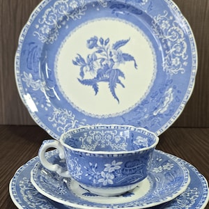 May include: A blue and white porcelain tea set featuring a floral design. The set includes a large plate, a teacup, a saucer, and a smaller plate. The edges of the plates and cup have a scalloped design.