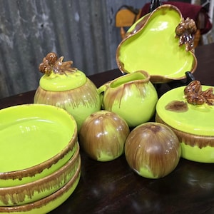May include: A collection of lime green ceramic serving dishes and containers with brown accents. The set includes bowls, a pitcher, a covered dish, and a pear-shaped platter. The lids and platter have decorative brown leaf-like handles.