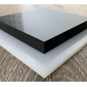 Pu&ograve; includere: Due pezzi quadrati di plastica, uno bianco e uno nero, impilati l'uno sull'altro. Il pezzo nero ha una superficie liscia e lucida.