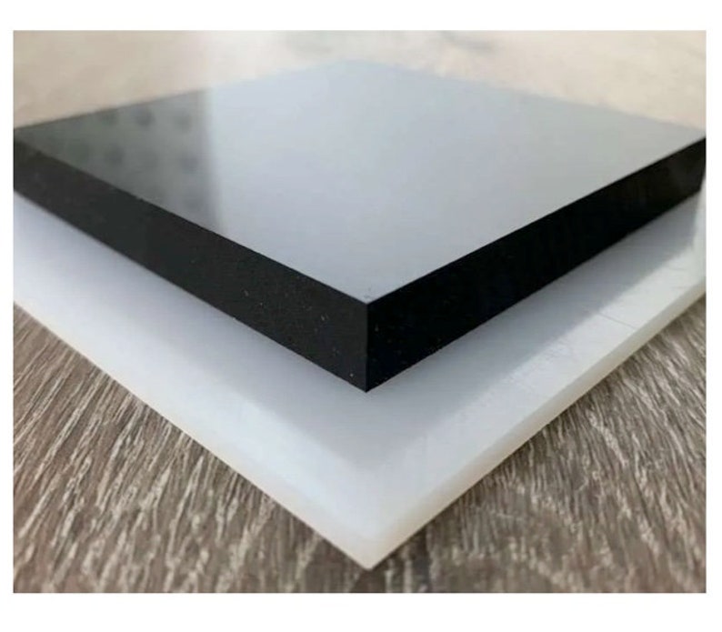 Pu&ograve; includere: Due pezzi quadrati di plastica, uno bianco e uno nero, impilati l'uno sull'altro. Il pezzo nero ha una superficie liscia e lucida.