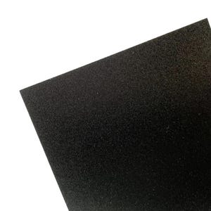 May include: A close-up shot of a black, textured sheet of material. The material appears to be a dense foam or felt, with a slightly uneven surface. The sheet is angled, revealing its thickness and the texture of the material.