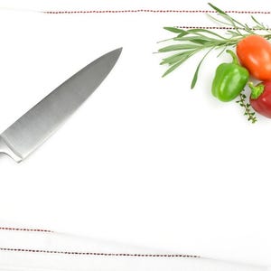 May include: A white kitchen towel with red stripes, a chef's knife, and a sprig of rosemary with red and green bell peppers.