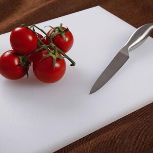 May include: White plastic cutting board with a silver knife and a cluster of red tomatoes on a vine.