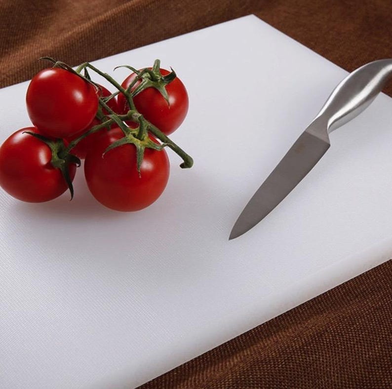 May include: White plastic cutting board with a silver knife and a cluster of red tomatoes on a vine.