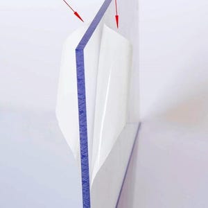 May include: Close-up of a clear, rectangular sheet with a blue edge, partially covered by a white protective film. The text "Double sided film masking" is visible at the top, with red arrows pointing to the film.