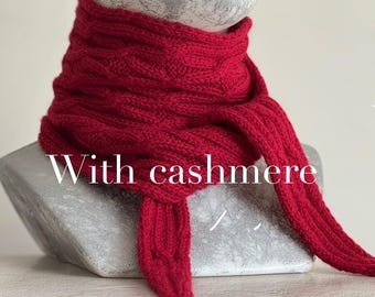 Może przedstawiać: Żywy czerwony dzianinowy szalik, narzucony na srebrny biust. Szalik wykonany jest z grubej, teksturowanej przędzy, z napisem "With cashmere" na zdjęciu. Końce szalika zwisają, prezentując jego długość i wzór.