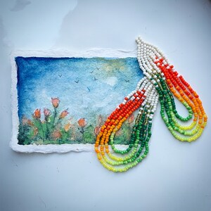 May include: A colorful beaded necklace with green, yellow, orange, and white beads. The necklace is made of multiple strands of beads and is arranged in a rainbow pattern.