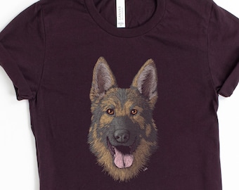 May include: A dark purple t-shirt with a detailed illustration of a German Shepherd dog's face. The dog has brown fur, black nose, and a pink tongue.