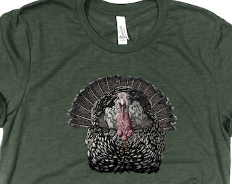 Könnte beinhalten: Ein grünes T-Shirt mit einem Aufdruck eines Truthahns mit ausgebreiteten Federn.