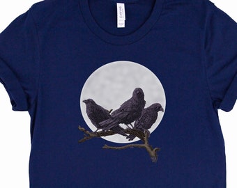 Könnte beinhalten: Ein marineblaues T-Shirt mit einem Motiv von drei schwarzen Raben, die auf einem Ast vor einem Vollmond sitzen.