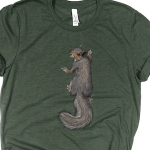 May include: A green t-shirt featuring a graphic of a grey squirrel climbing a tree. The squirrel is facing away from the viewer.