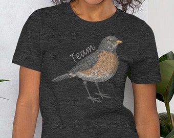 May include: A dark heather grey t-shirt with a robin illustration and the word "Team" printed on the front.