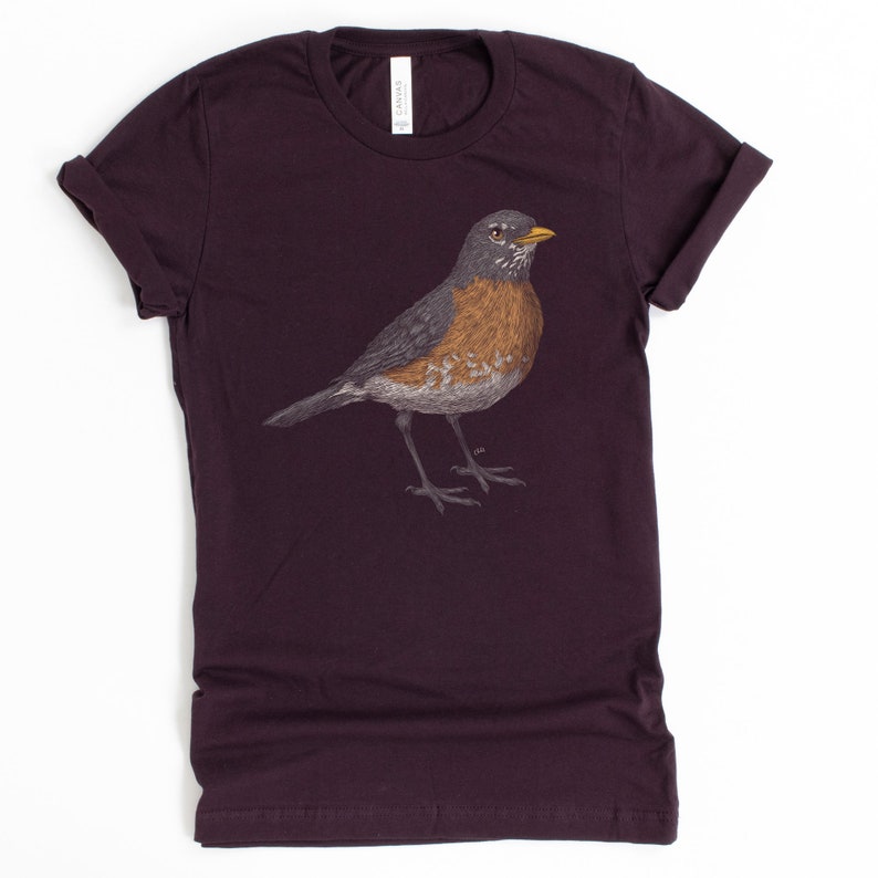 May include: A dark purple t-shirt with a detailed illustration of a robin bird in the center.
