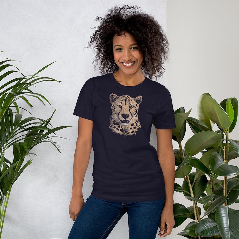 May include: A navy blue t-shirt with a graphic print of a cheetah's face. The cheetah has a spotted coat and a serious expression.