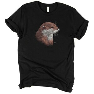 May include: A black t-shirt with a brown and gray otter illustration on the front. The otter is looking to the right and has a small signature in the bottom right corner.
