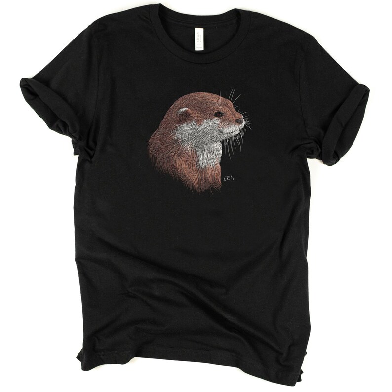 May include: A black t-shirt with a brown and gray otter illustration on the front. The otter is looking to the right and has a small signature in the bottom right corner.
