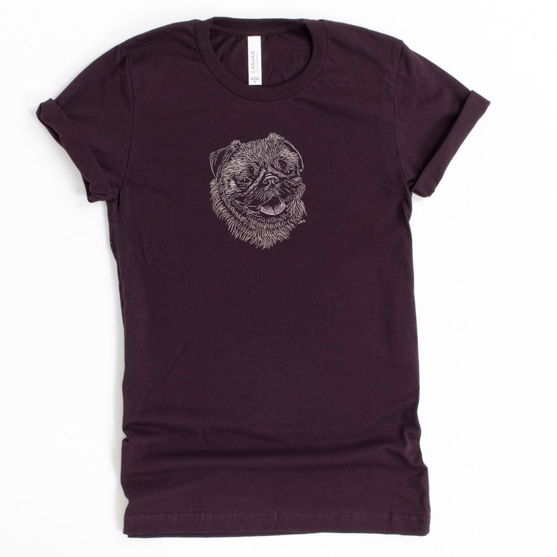 Puede incluir: Una camiseta de color morado oscuro con un dibujo blanco de un rostro de carlino.