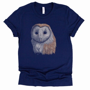 K&ouml;nnte beinhalten: Ein marineblaues T-Shirt mit einer Illustration einer wei&szlig;en und braunen Scheune Eule auf der Vorderseite.